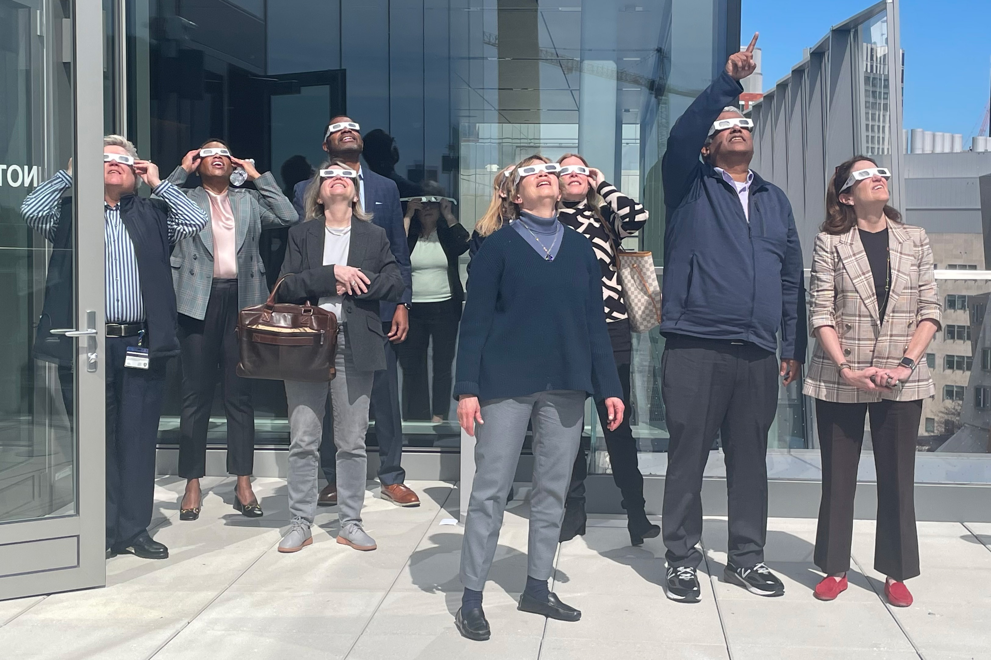 MIT members, including President Sally Kornbluth, look up at the eclipse from a balcony.